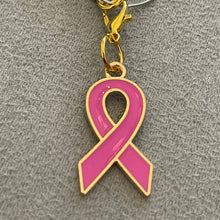 Load image into Gallery viewer, A pink ribbon charm attached to a gold-colored ring, designed as a mobile dust plug or backpack zipper pull.