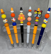 Load image into Gallery viewer, Colorful pens with decorative beads on a clear stand against a gray background