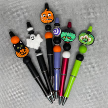 Load image into Gallery viewer, Set of Halloween-themed pens with colorful pen toppers on a textured surface.
