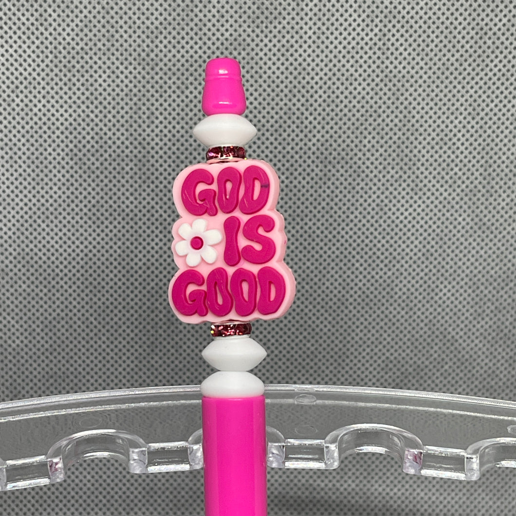 Pink pen with 'GOD IS GOOD' text on a clear stand against a gray background