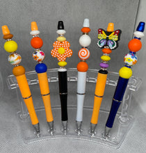 Load image into Gallery viewer, Colorful pens with decorative beads on a clear stand against a gray background
