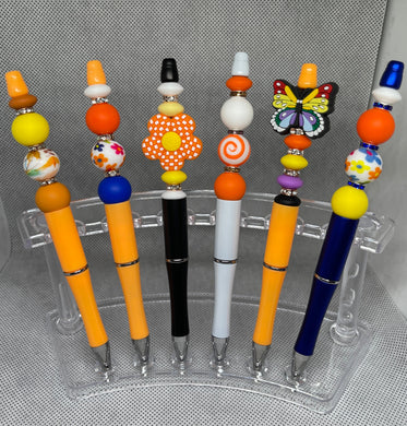 Colorful pens with decorative beads on a clear stand against a gray background