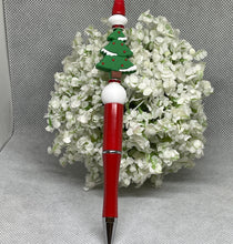 Load image into Gallery viewer, Red pen with a Christmas tree design on top, held over a bouquet of white flowers.
