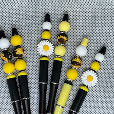 Set of decorative pens with yellow, white, and black beads on a textured gray background