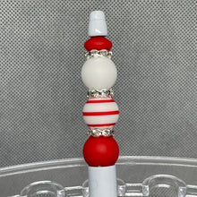 Load image into Gallery viewer, Decorative pen top with red, white, and silver beads on a clear stand against a gray background
